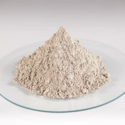 Pile of light grey bentonite-cement powder grout on a glass dish for use in geotechnical and sealing applications