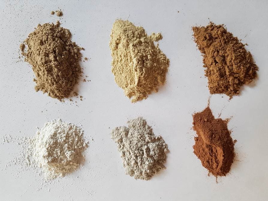 A range of bentonite powders in different natural colours, illustrating mineral variation by source location.