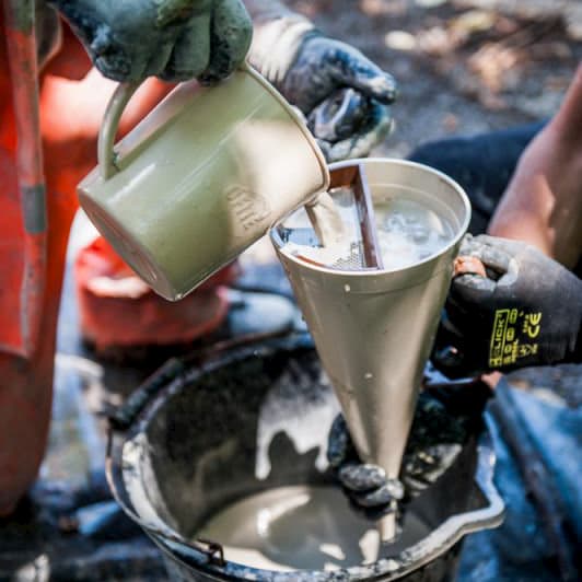 On-site viscosity test of bentonite drilling slurry using a Marsh funnel, with construction workers handling the mix