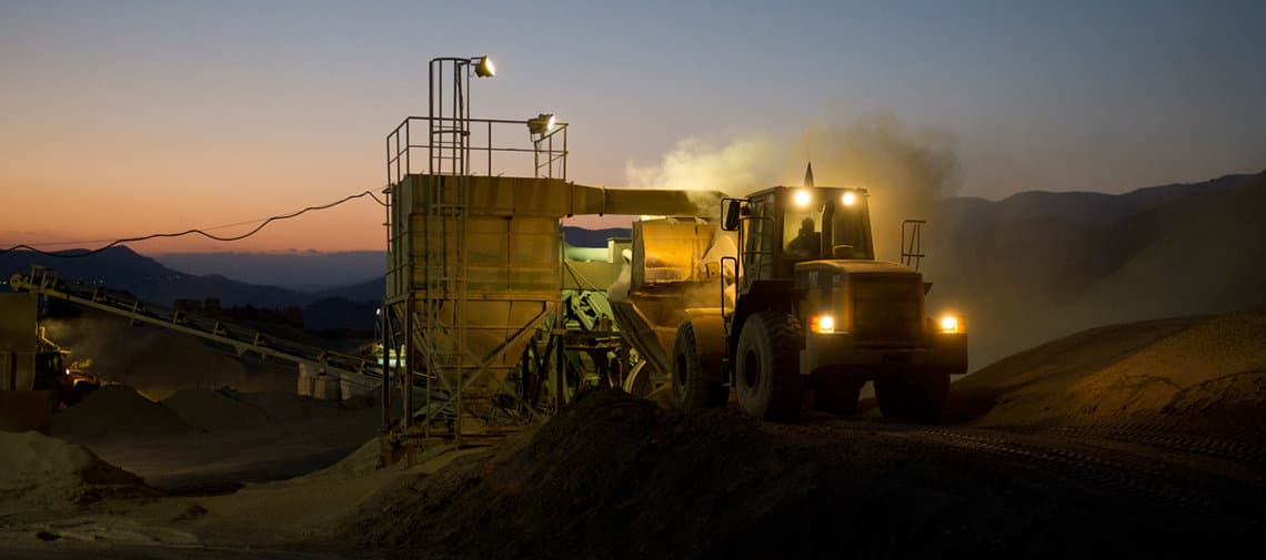 Heavy machinery operating at a mineral processing quarry during sunset, loading bulk industrial materials